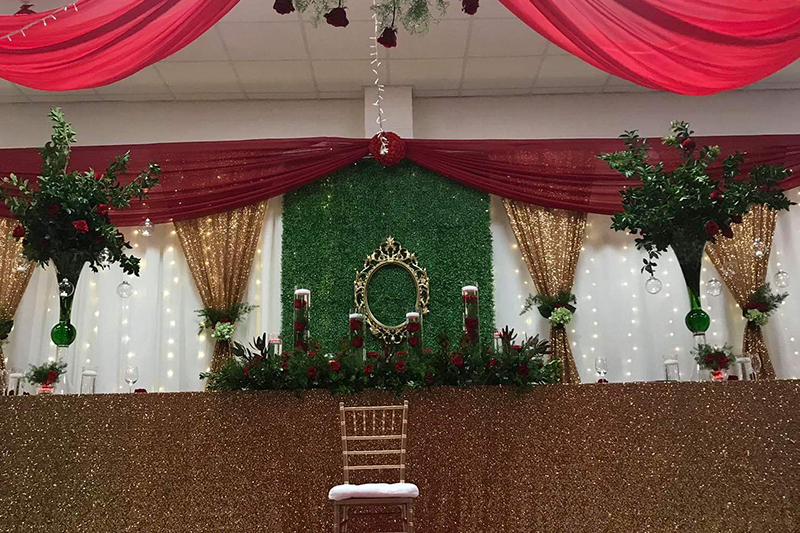 Red and gold sweetheart stage with greenery wall and gilded frame